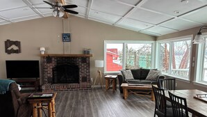 A spacious living room with a brick fireplace, a television, a sofa, and a dining area with wooden furniture.