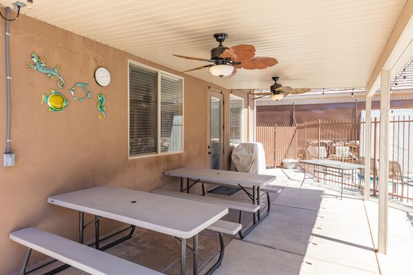 A covered patio area with picnic tables, ceiling fans, and decorative wall art.