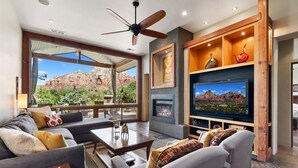 A spacious living room with a fireplace, a large flat-screen TV, and a view of red rock formations. - Beauty and the Beast Stunning Home, Stunning Views, Walk to Town Weekly Discount (Sedona)