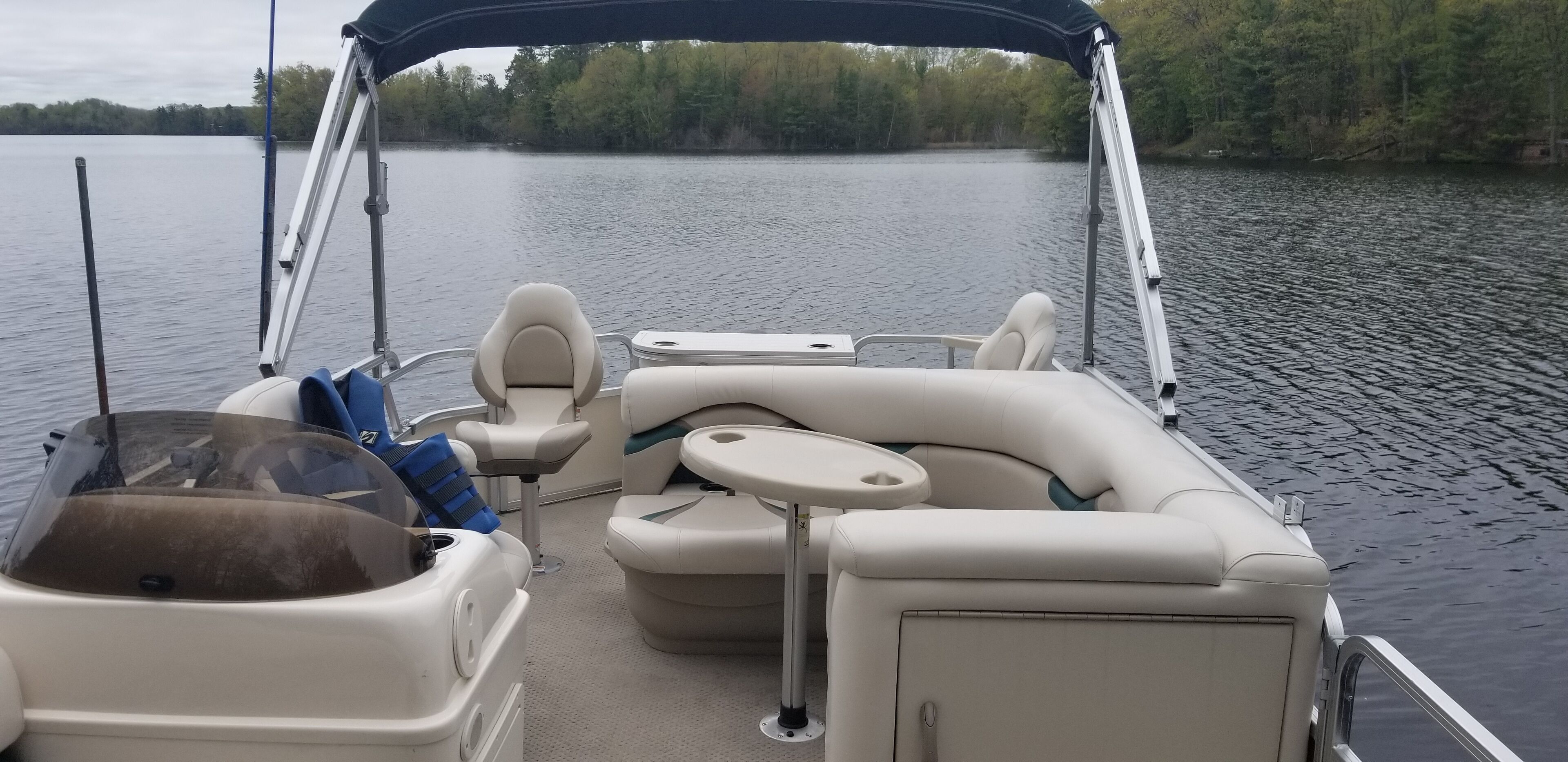 L'intérieur d'un bateau, avec des sièges et une table, entouré d'une eau calme et d'arbres.
