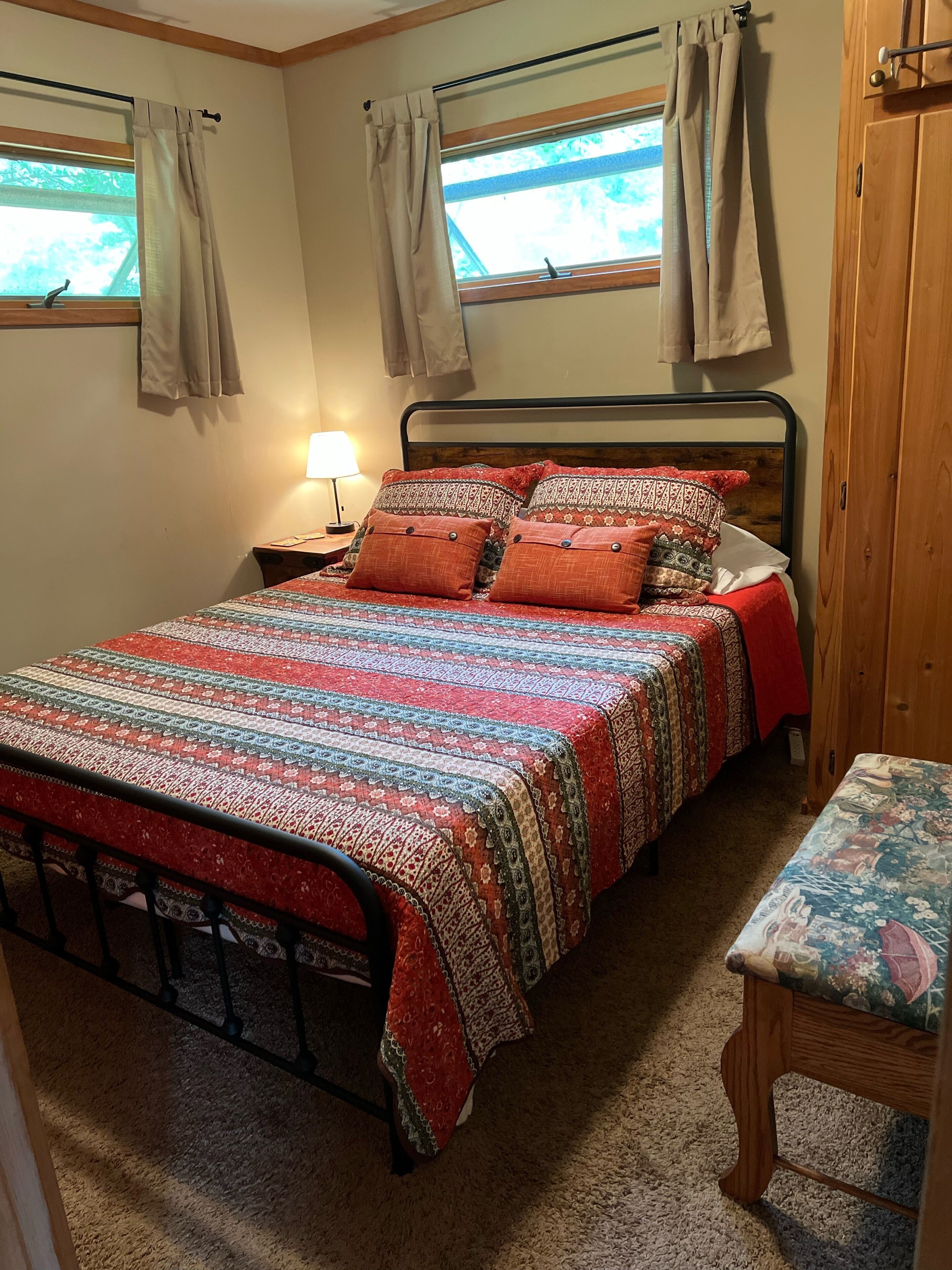 A bedroom with a bed, a nightstand, a lamp, a window with curtains, and a wooden door.