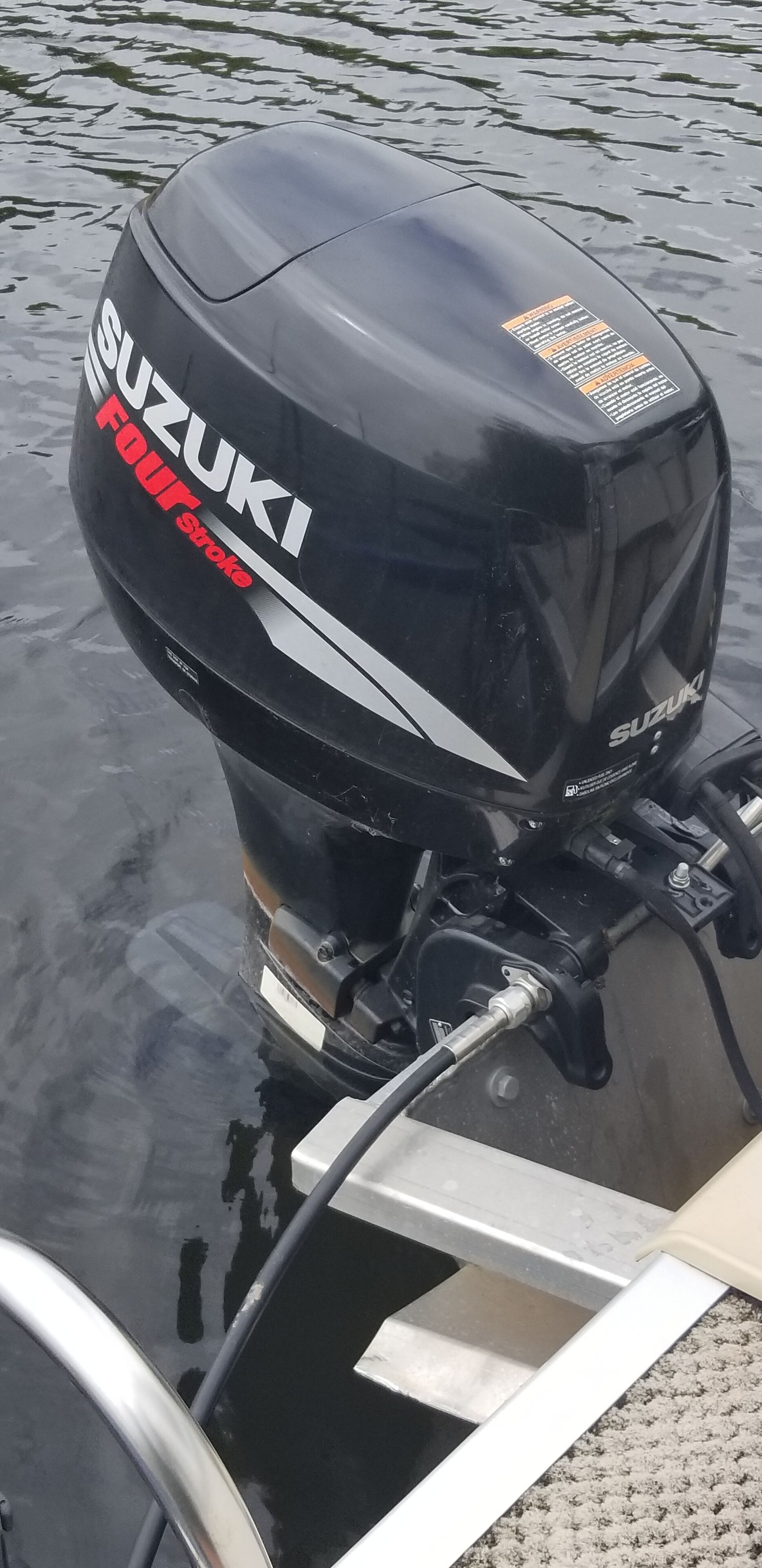 Motor fueraborda Suzuki de cuatro tiempos, negro, sujeto a una lancha.