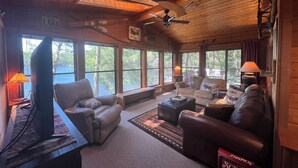 A cozy cabin interior with a fireplace, comfortable seating, and large windows offering views of the lake.