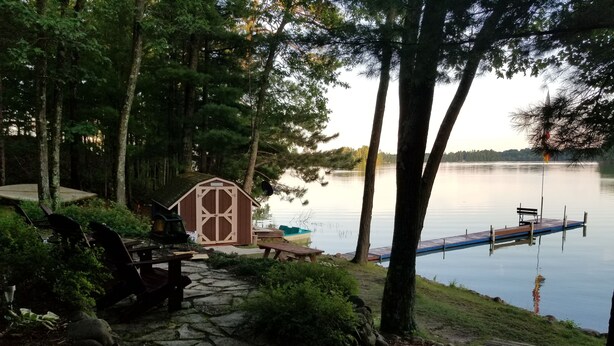 A lakeside cabin with a dock, stone pathway, and picnic table.