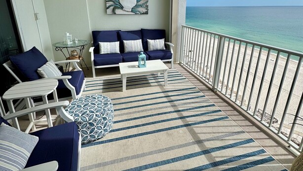 Ein Balkon mit Blick auf das Meer, ausgestattet mit einer Couch, Sesseln, einem Tisch und einem Deckenventilator.