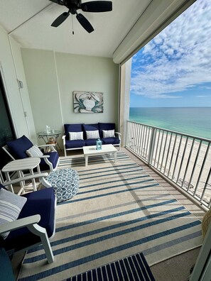 A balcony with a view of the ocean, featuring a sofa, chairs, a table, and a ceiling fan. - Regency Isle PH1110 Luxurious  Beachfront Condominium (Orange Beach)