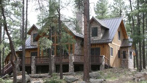 Une cabane en rondins, avec des fondations en pierre, un revêtement extérieur en bois et un toit en métal, entourée d’arbres et de rochers.