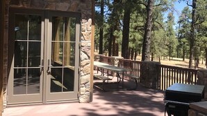 Un bâtiment en pierre doté d’une porte et de fenêtres en verre, d’une terrasse couverte avec des tables de pique-nique et d’un barbecue.