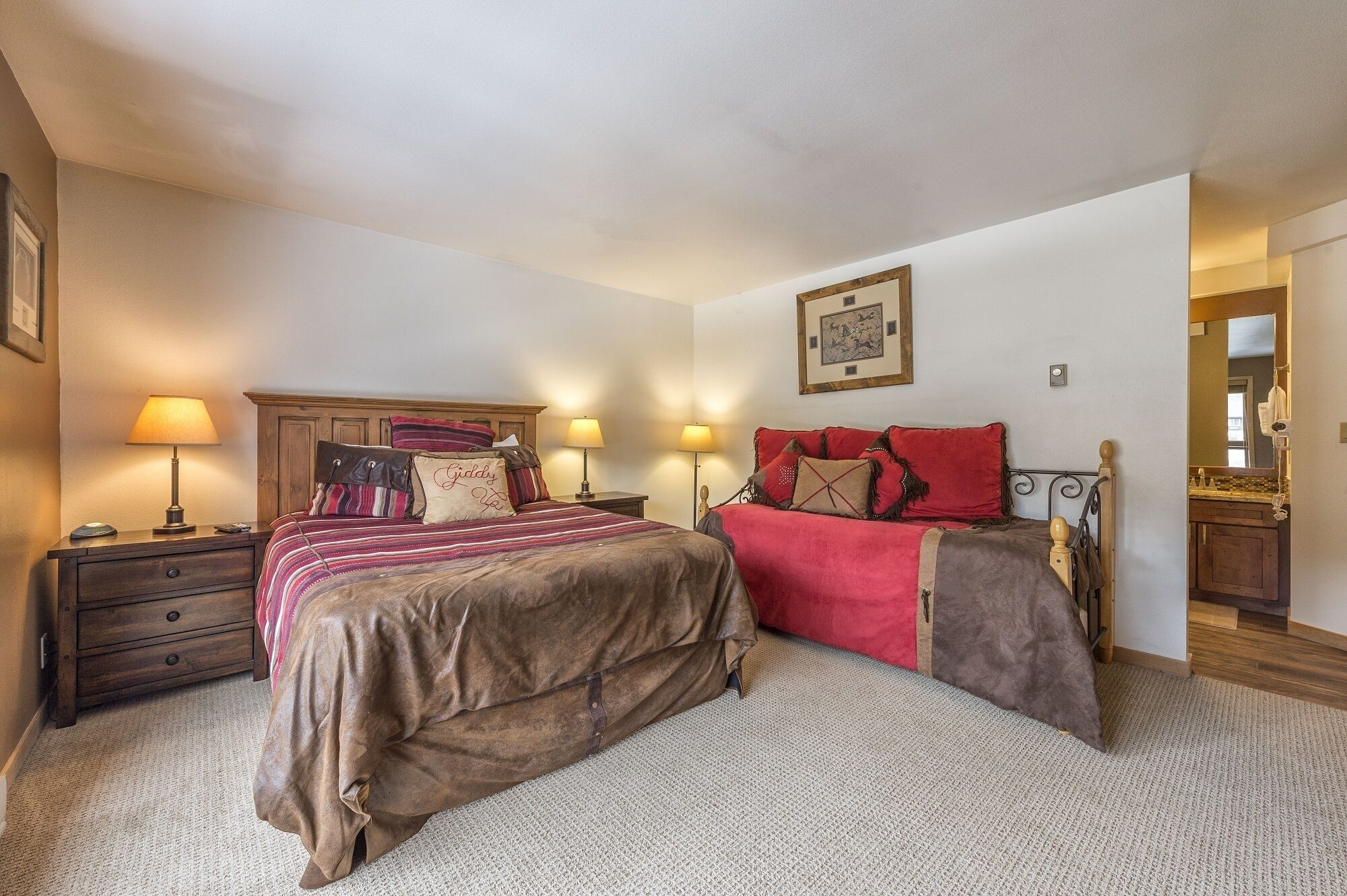 A bedroom with two beds, a wooden headboard, bedside lamps, a framed picture on the wall, and a wooden dresser.