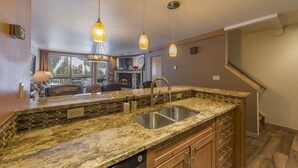 A kitchen with granite countertops, a double sink, and pendant lighting.