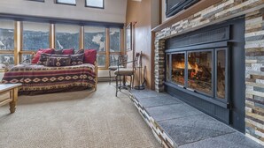 A cozy room with a large bed, a fireplace, and a view of the mountains through large windows.