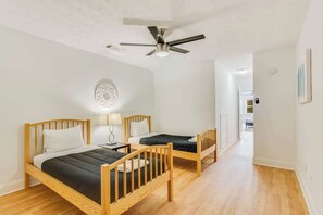 A room with two wooden beds, a ceiling fan, a round wall decoration, and a hallway leading to another room.