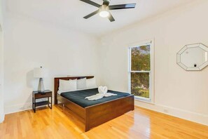 A bedroom with a bed, a nightstand, a ceiling fan, a window, and a wall-mounted mirror. - Pool retreat for groups, sleeps 12 (Conyers)