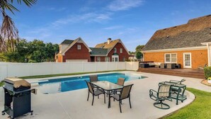 A backyard with a swimming pool, outdoor furniture, and a barbecue grill.
