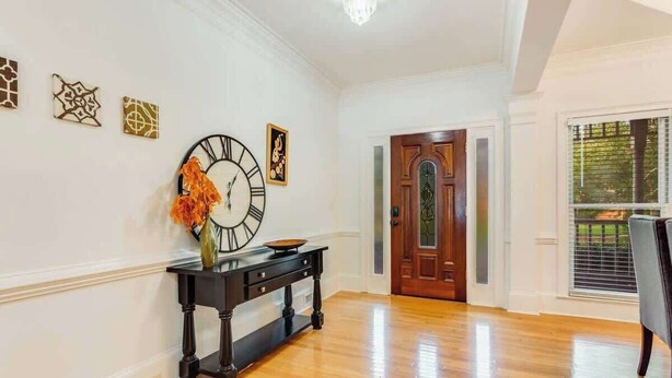 A hallway with a wooden floor, a black console table with a clock, and a door with a decorative glass panel.