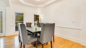A dining room with a round table, grey upholstered chairs, and a chandelier.