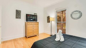 A bedroom with a bed, a dresser, a TV, and a window with blinds.