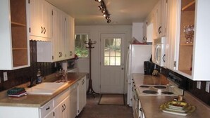 Una cocina con armarios blancos, estufa, refrigerador y pileta.