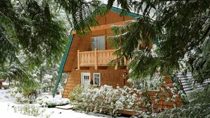 Una cabaña de madera con balcón, rodeada de árboles cubiertos de nieve.