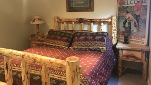 Una habitación rústica con una cama de madera, un cartel de bienvenida enmarcado y una lámpara.