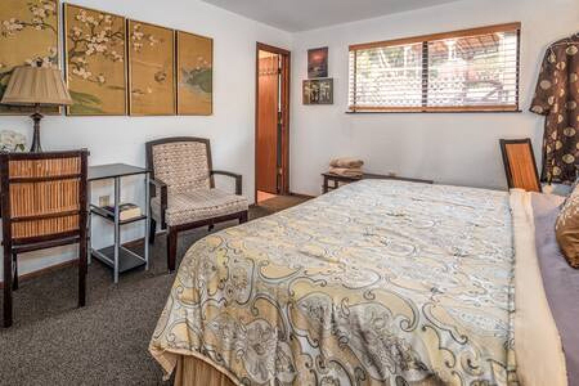 A bedroom with a bed, a chair, a desk, and a window with blinds.