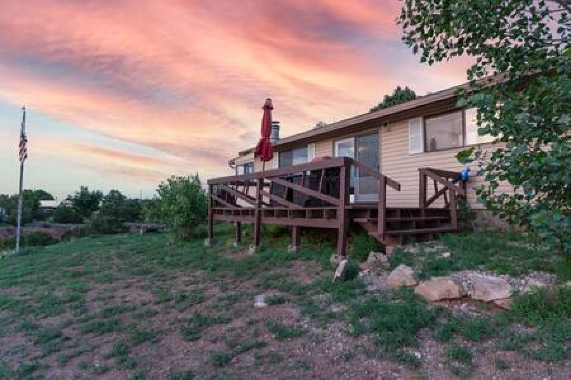 A single-story house with a deck, surrounded by a grassy area with rocks.