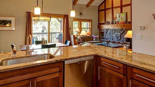 Una cocina con armarios de madera, encimeras de granito y lavavajillas empotrado. Hay luces colgantes, una ventana con cortinas y un salpicadero de piedra.