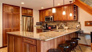Una cocina moderna con armarios de madera, electrodomésticos de acero inoxidable, encimeras de granito e iluminación colgante.