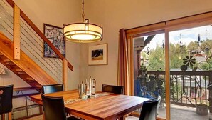 Un comedor con mesa y sillas de madera, un lámpara colgante y vistas al exterior a través de un ventanal.