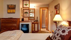 Habitación de hotel con una cama, un escritorio con computadora, televisión, lámpara y puerta que da a otra habitación.