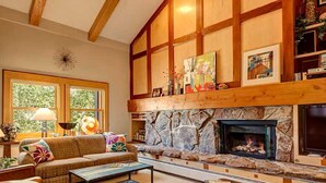 Una sala de estar acogedora con chimenea de piedra, vigas de madera y un amplio ventanal.