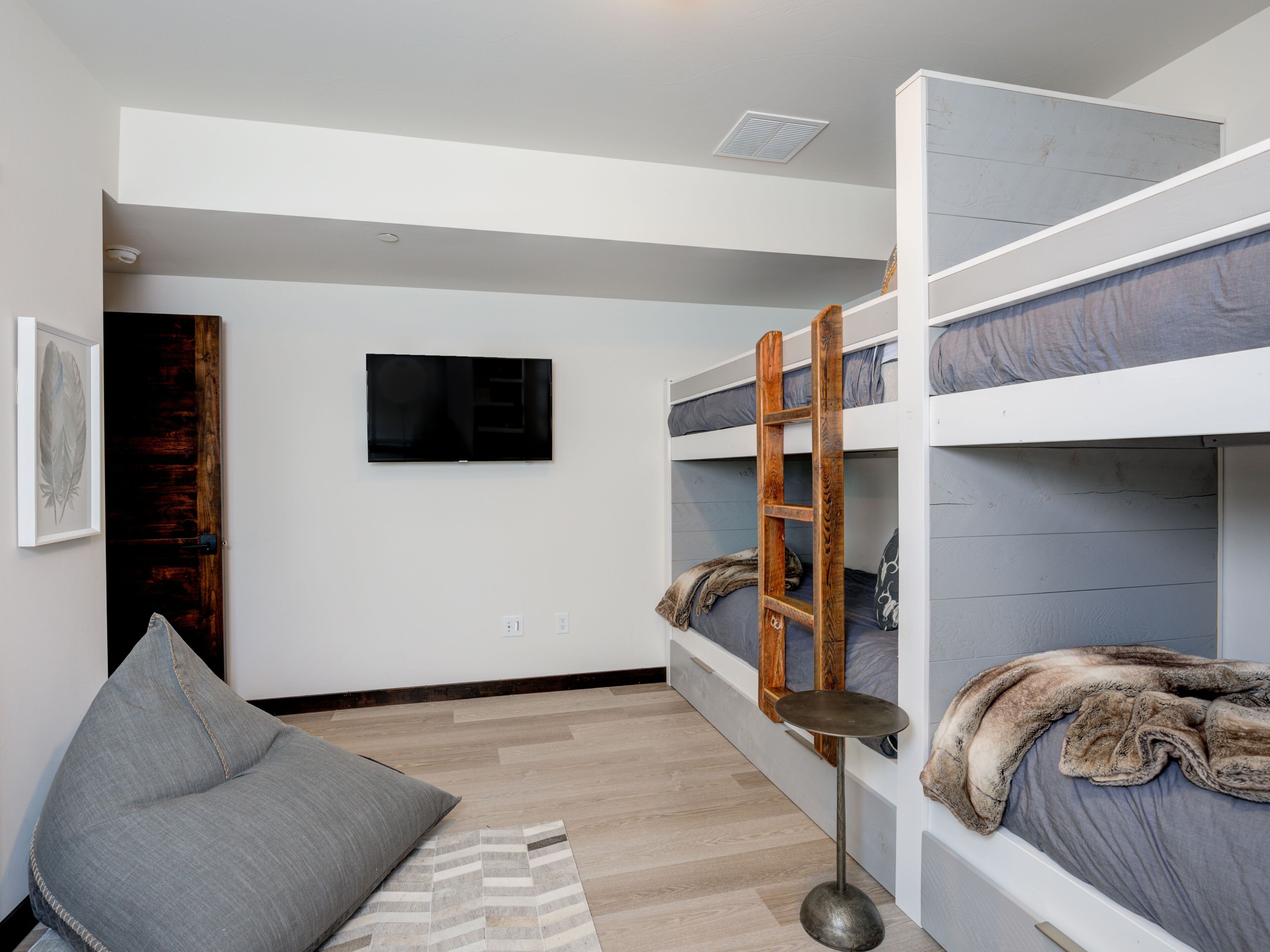 A bunk bed room with a television, a wooden ladder, and a grey pillow.