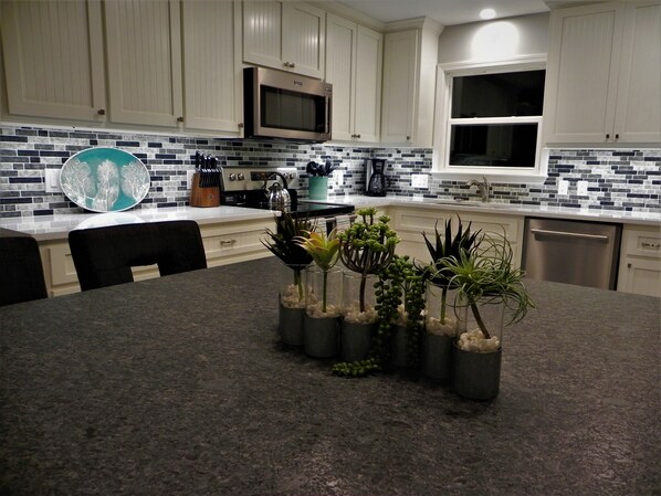 A kitchen with white cabinets, a microwave, a coffee maker, and a window. There are plants on the counter and a knife block.