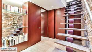 A modern interior with a wooden staircase, a glass shelf with books, and a stone wall.