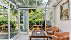 A conservatory with glass walls, wicker furniture, and a table with a magazine.