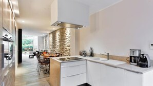 A modern kitchen with white cabinetry, a stone accent wall, and a dining area with a table and chairs.