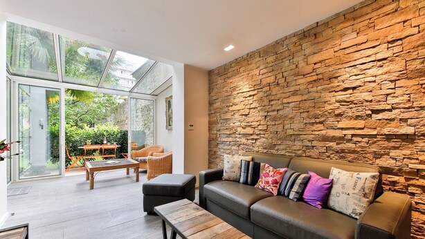 A modern living room with a stone wall, leather sofa, and glass doors leading to a patio.