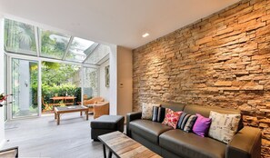 A modern living room with a stone wall, leather sofa, and glass doors leading to a patio. - Amazing Haven Of Peace Near Eiffel Tower, 1000sqf With Private Terrace On Garden (Paris)