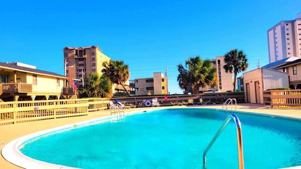 A swimming pool with a metal ladder, surrounded by palm trees and buildings. - On the Beach! 2BR/1B - Low Rise/Low Rates - Steps to the sand-Gulf Village 209! (Gulf Shores)
