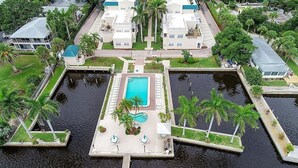 An aerial view of a waterfront property with a central swimming pool, palm trees, and a dock.