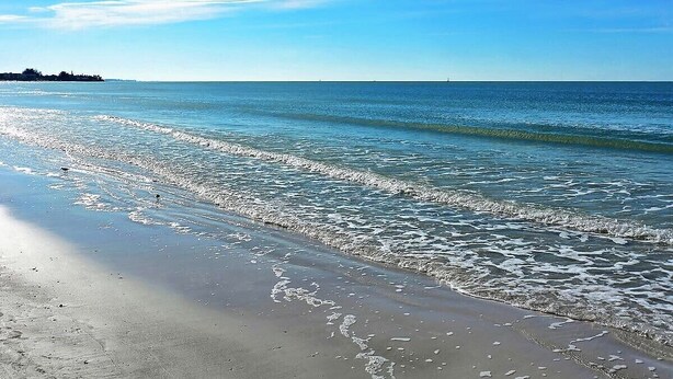A beach with clear water, a sandy shore, and a distant landmass.