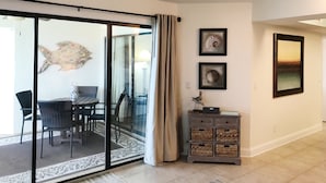 A room with a sliding glass door leading to a dining area, a small cabinet with baskets, and two framed pictures on the wall.