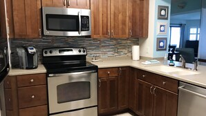 A kitchen with wooden cabinets, stainless steel appliances, a tiled backsplash, and a view of the living area.
