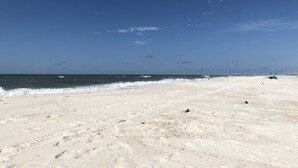 Ampia spiaggia sabbiosa con onde calme e cielo azzurro terso.