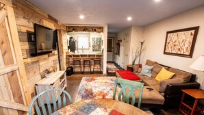 A cozy living room with a wooden wall, a TV mounted above a wooden table, a sofa with cushions, and a colorful rug. - Ski, Hike, Fun - Great Location!!  Perfect 2 Br/2 Ba Condo! (Brian Head)