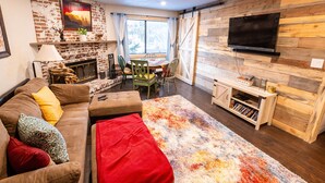 A cozy living room with a fireplace, a TV mounted on a wooden wall, and a dining area with a table and chairs. - Ski, Hike, Fun - Great Location!!  Perfect 2 Br/2 Ba Condo! (Brian Head)