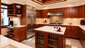 A modern kitchen with wooden cabinets, a stainless steel refrigerator, a built-in wine rack, and a central island with a marble countertop. - Plaza Lodge | 7 - 4 Bedroom Gold with private rooftop Jacuzzi (Vail)