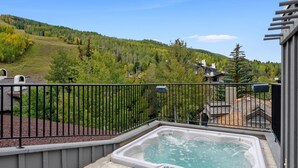 A hot tub on a balcony with a view of a forested hillside. - Plaza Lodge | 7 - 4 Bedroom Gold with private rooftop Jacuzzi (Vail)