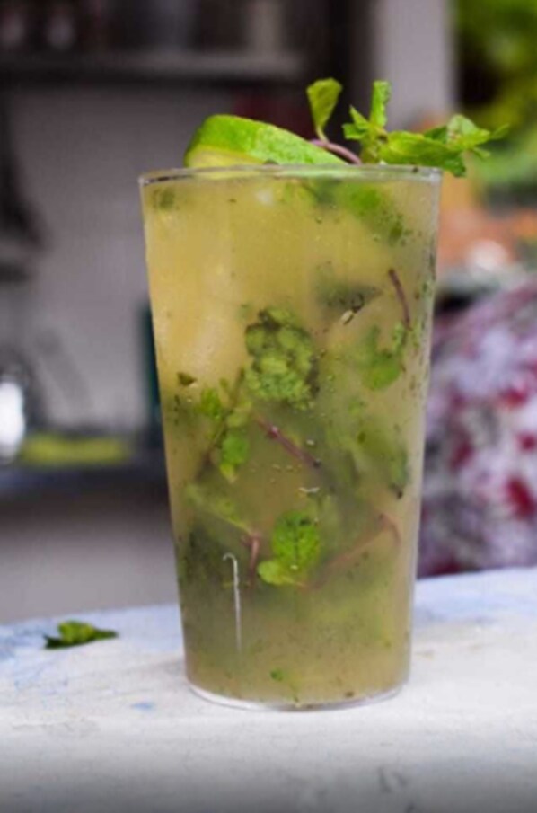 A clear glass with a beverage, garnished with mint leaves.