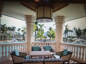 A covered outdoor seating area with a table and chairs, overlooking a pool and palm trees. - Marriott Kauai Beach Club, Ocean View Studio.  Available Christmas Week! (Lihue)